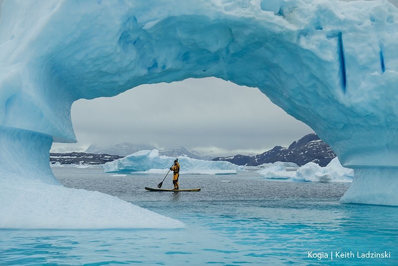 Paddleboarder under an iceberg arch